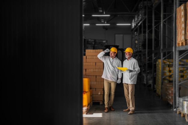 Father and son standing in their warehouse with helmets on their heads and looking at package prepared for transport. looking proud and satisfied. Premium Photo